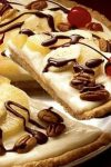 This Banana Split Dessert Pizza is the perfect dessert for any celebration. A sugar cookie crust topped with cream cheese frosting, fruit, nuts, and chocolate sauce!