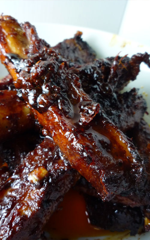 Pork spare ribs in a white dish. The image is zoomed in to highlight the glaze and caramelization.