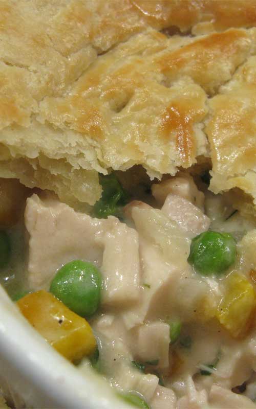 Top view of a chicken pot pie. Part of the crust is removed to show the chicken, carrots, and peas inside.