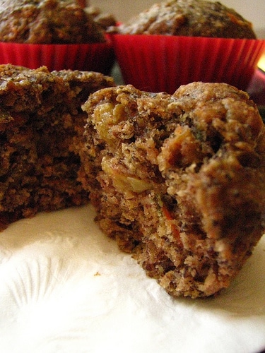 Close up view of a Flax and Oat Bran Muffin that has been split open. There are two more muffins with red liners in the backgroiund.