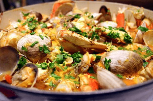 An enamled pot filled with Seattle-style Cioppino; showing clams, crab, parsley, and green onion.