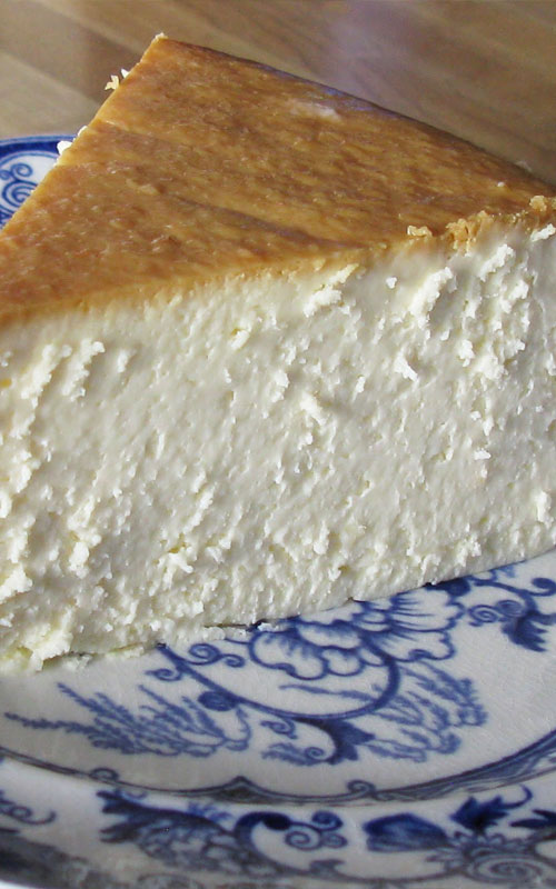 A slice of New York Cheesecake on a white and blue plate, showing the interior texture of the cheesecake.
